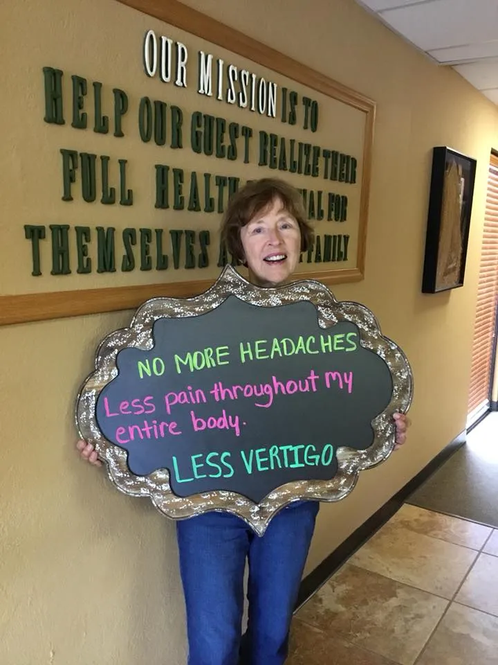 Patient in the Ennis Chiropractic office holding a sign reading no more headaches, less pain, less vertigo